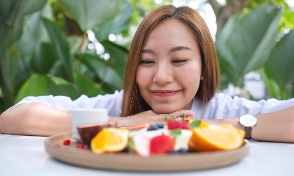 Close-up of a young woman looking at a colorful plate of mixed fruits, symbolizing a holistic approach to eating disorder recovery.