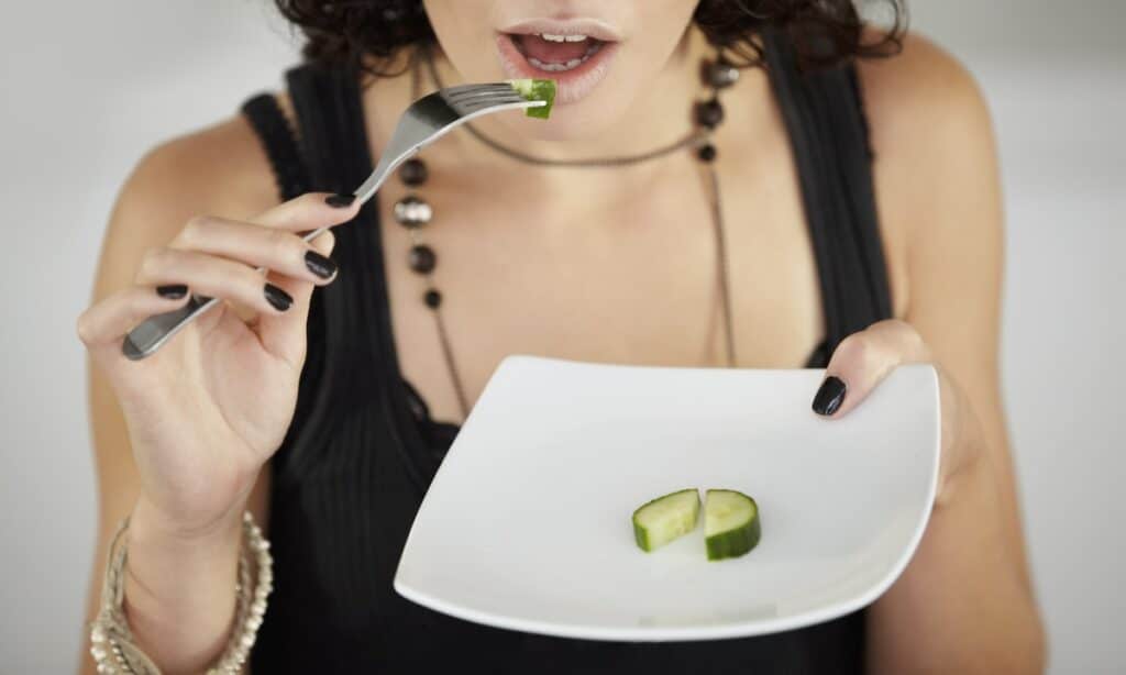 Woman holding a plate with a single slice of cucumber, representing dietary restrictions associated with OSFED.