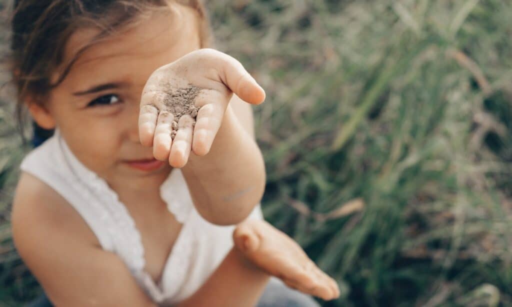 Child holding a handful of soil, illustrating the condition of Pica, where individuals eat non-food items.
