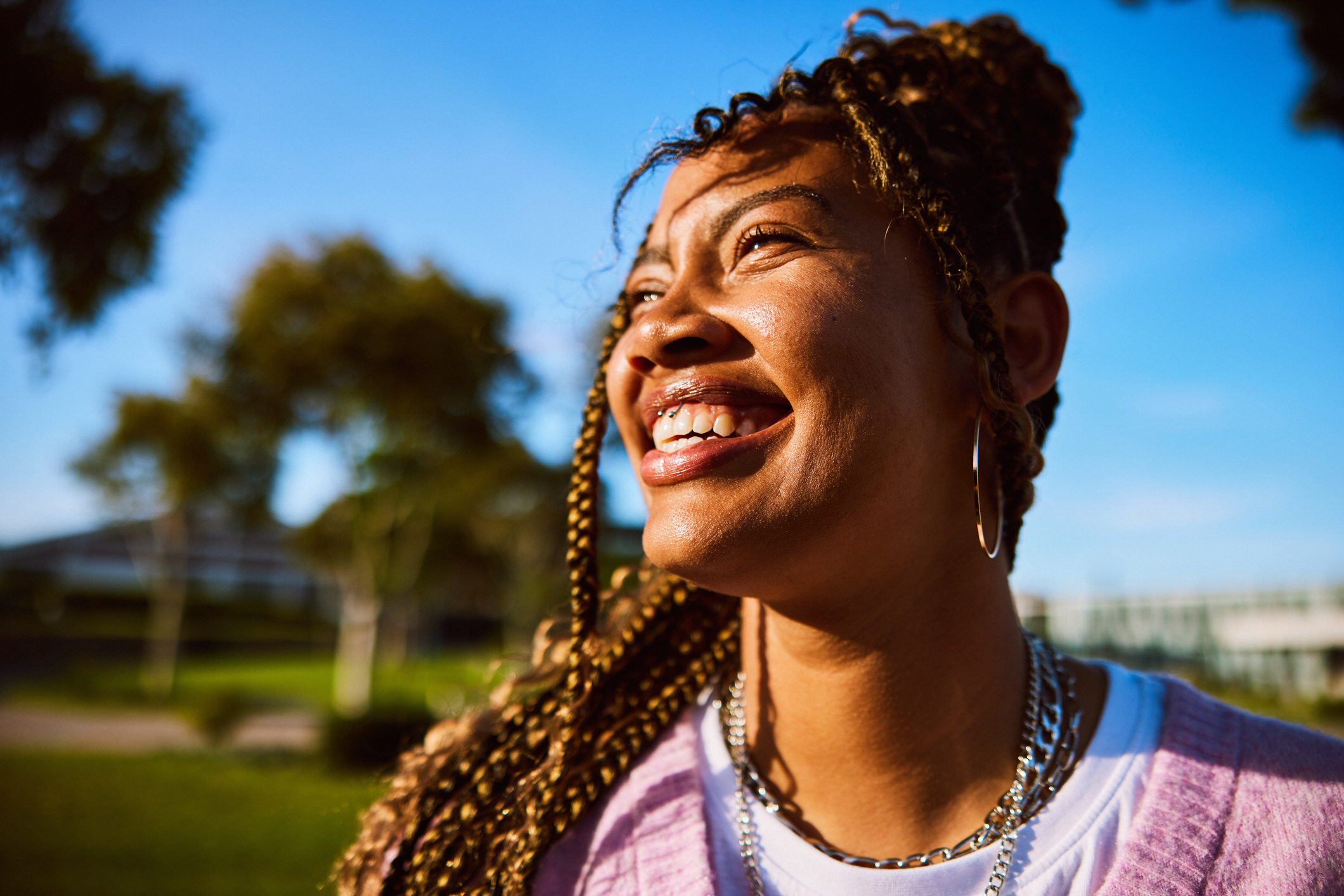 Headshot of young woman with braided hair looking away, toothy smile Head and shoulders of cheerful young woman against blue sky, laughing
