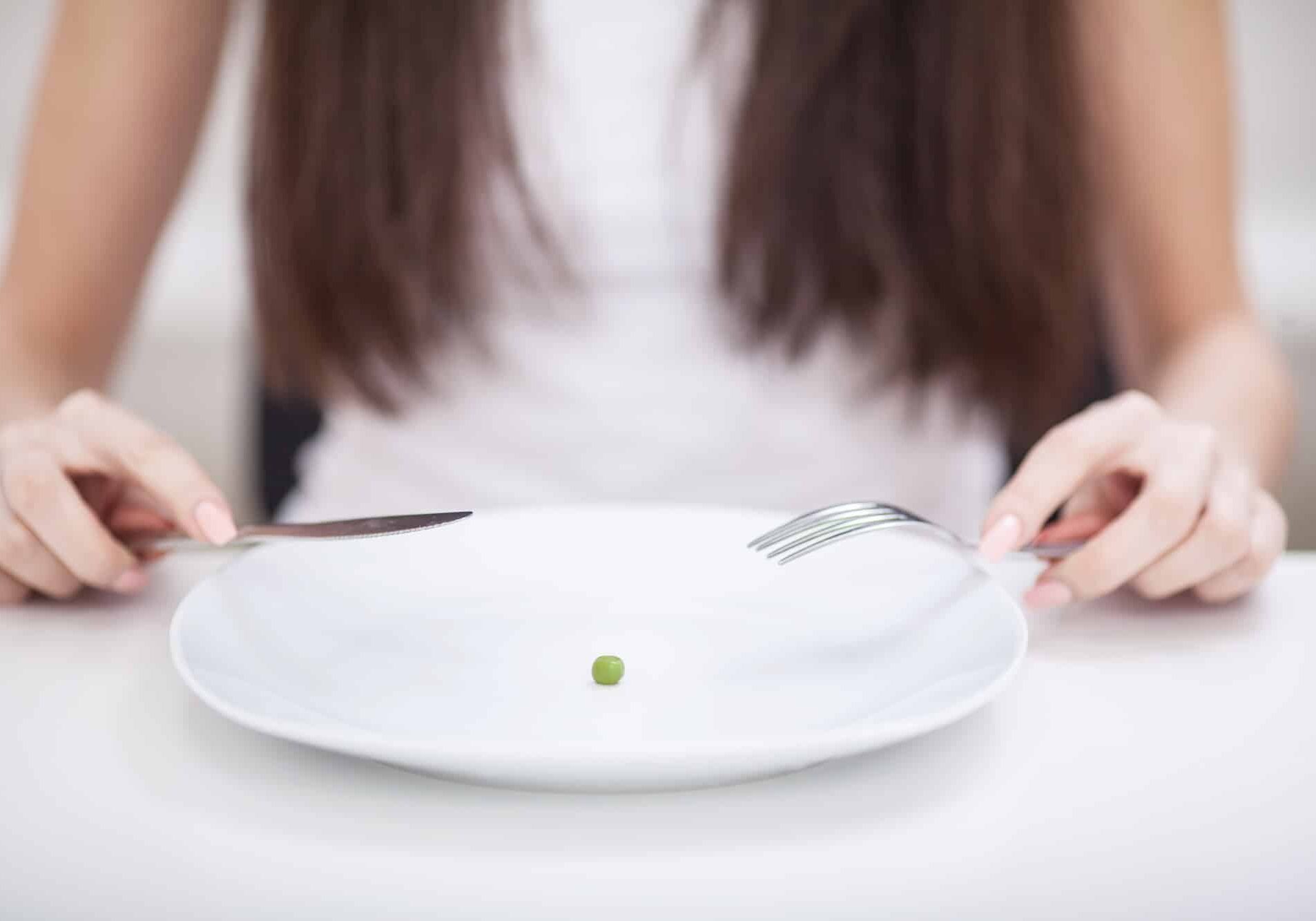 Diet. Suffering from anorexia. Cropped image of girl trying to put a pea on the fork Diet. Suffering from anorexia. Cropped image of girl trying to put a pea on the fork