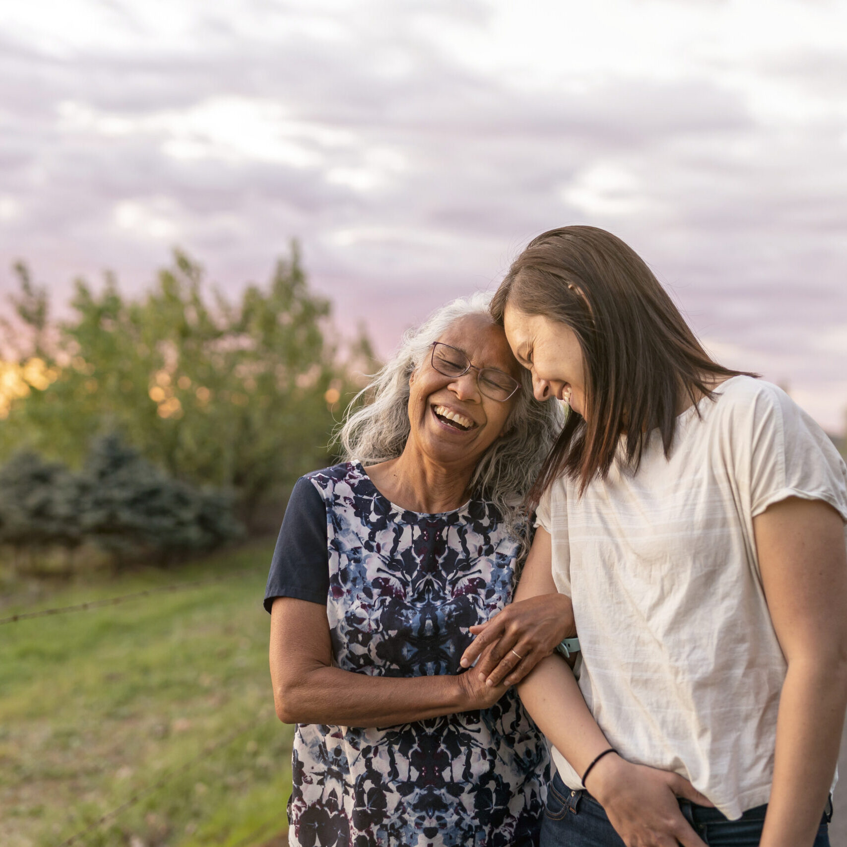 A beautiful senior mom of pacific island descent is walking outdoors with her adult thirty something year old daughter. They are enjoying each others company and soaking in the gorgeous, colorful, sunset.