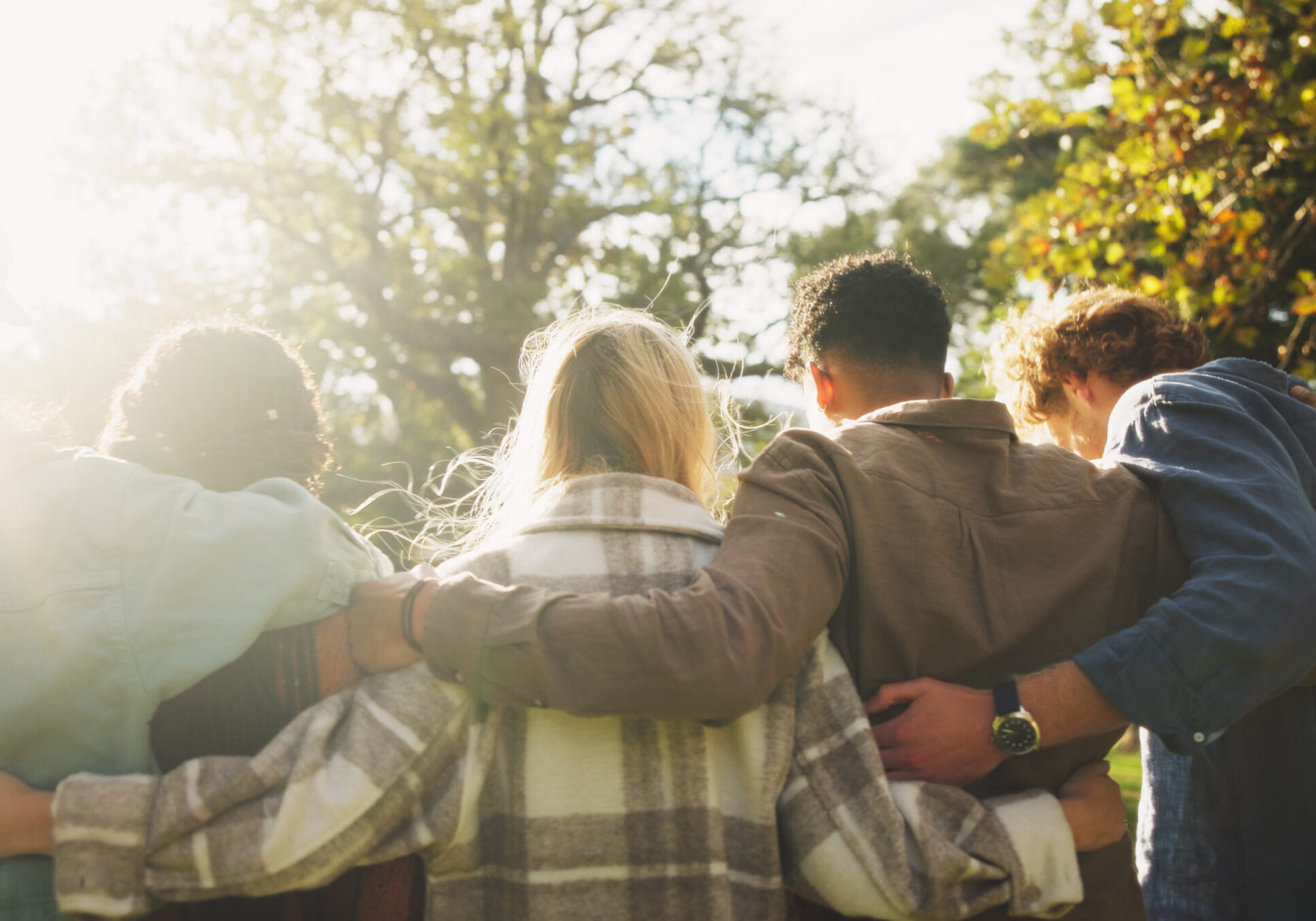 Group, back and friends to relax outdoor on school break, discussion and hug for bonding in summer. People, students and embrace with support, care and trust together for social reunion at park