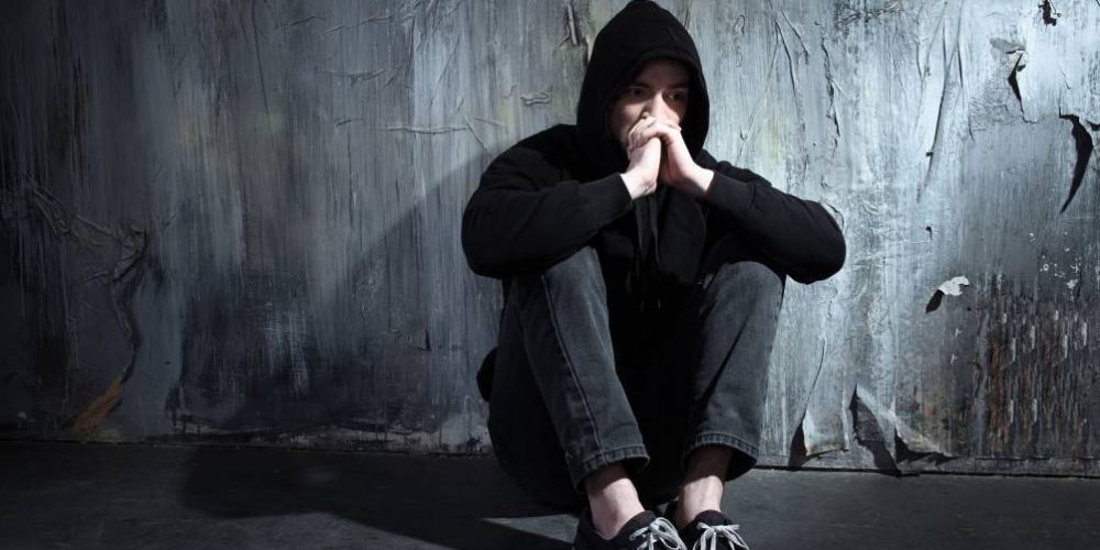 Photo of desperate young drug addict wearing hood and sitting alone in dark meth addiction treatment